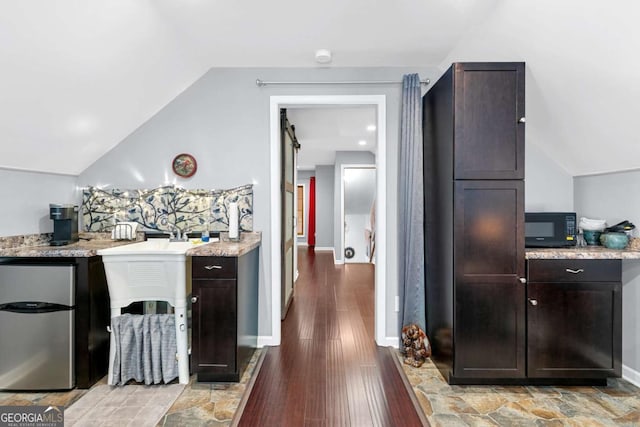 bar featuring black microwave, refrigerator, lofted ceiling, light wood finished floors, and baseboards
