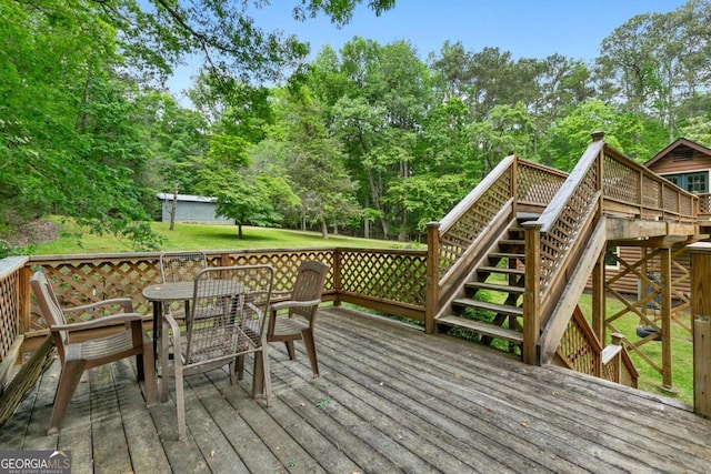 wooden terrace featuring stairs, outdoor dining area, and view of wooded area