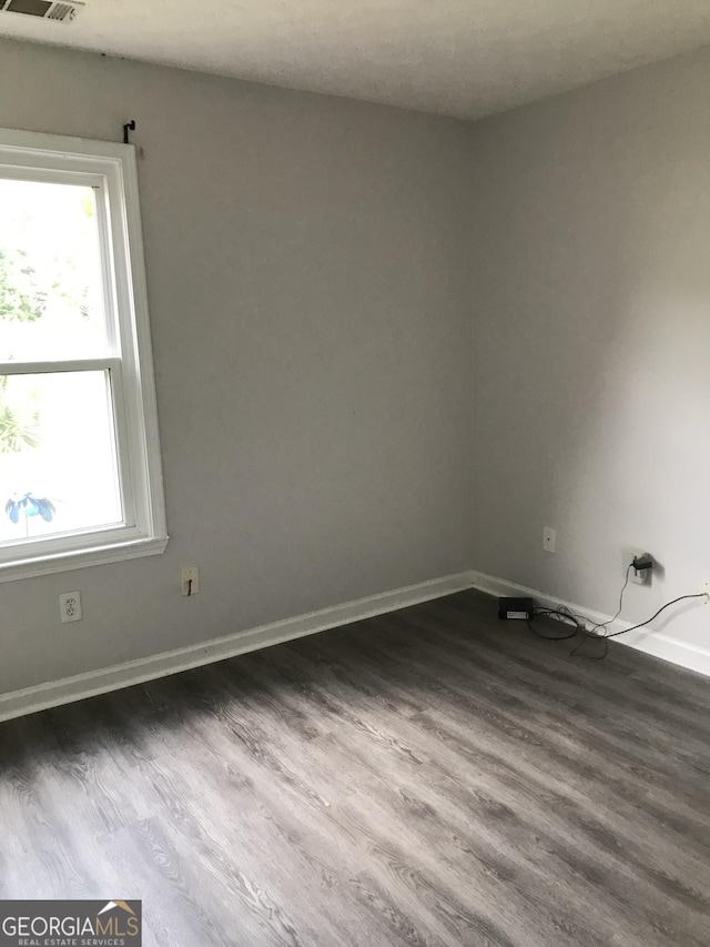empty room featuring baseboards, visible vents, and dark wood finished floors