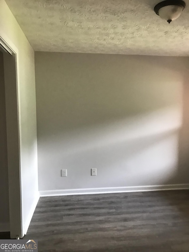 empty room featuring baseboards, dark wood-style flooring, and a textured ceiling