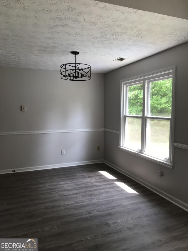 unfurnished dining area featuring a textured ceiling, visible vents, a chandelier, dark wood-style floors, and baseboards