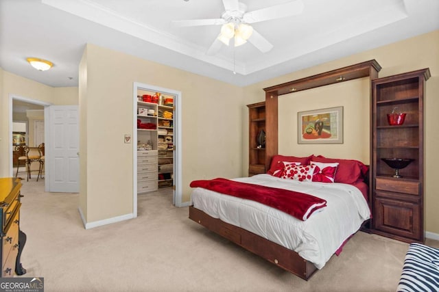 bedroom featuring a raised ceiling, light colored carpet, a walk in closet, a closet, and baseboards