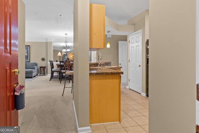 kitchen featuring a chandelier, a sink, light tile patterned floors, dark stone counters, and pendant lighting