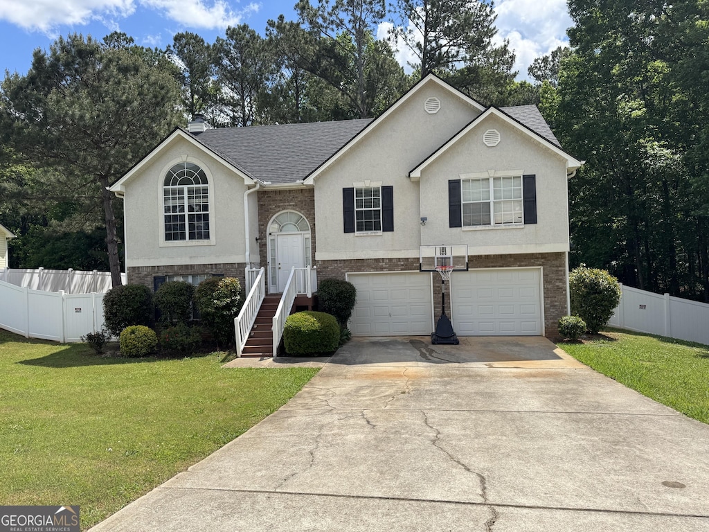 raised ranch with a front yard, stucco siding, an attached garage, and driveway