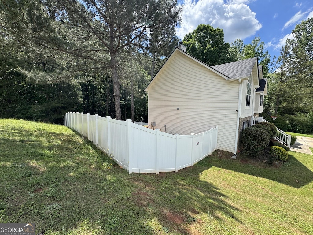 view of side of home featuring a chimney, a yard, roof with shingles, and fence