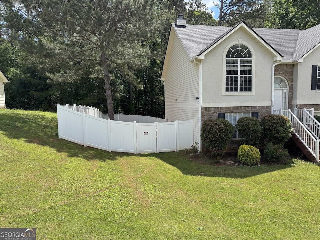 view of side of property with fence, roof with shingles, a chimney, and a lawn