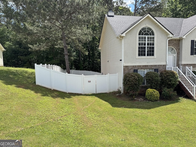 view of side of property with fence, roof with shingles, a chimney, and a lawn