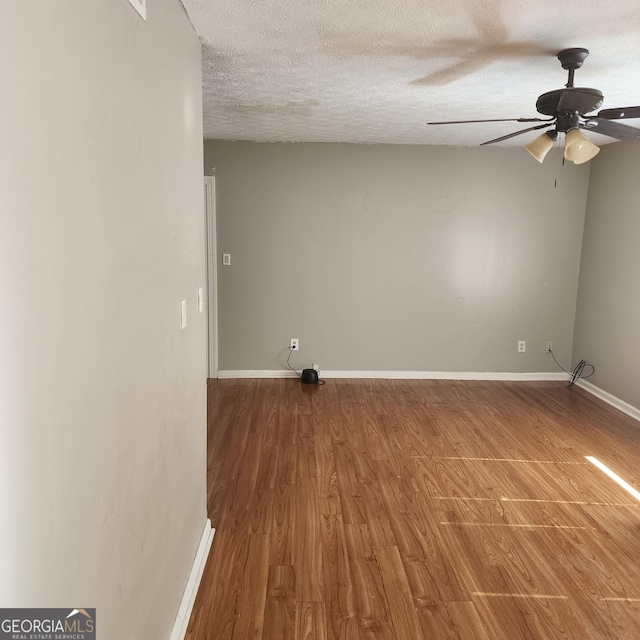 empty room with a ceiling fan, baseboards, a textured ceiling, and wood finished floors