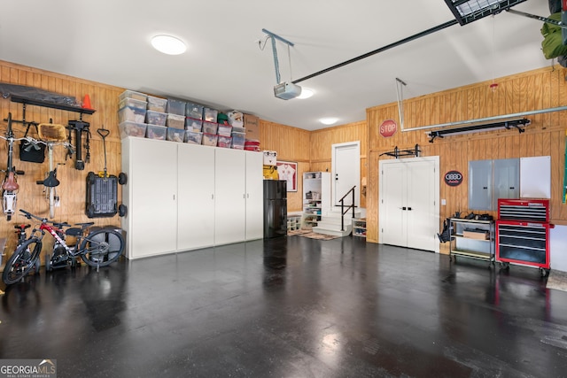 garage featuring freestanding refrigerator, wood walls, a garage door opener, and electric panel