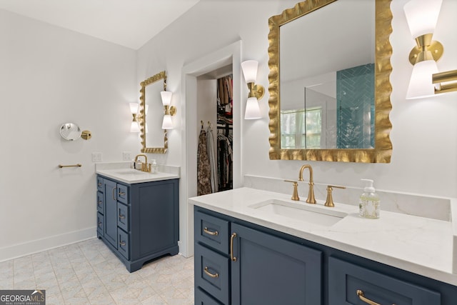 full bath featuring baseboards, walk in shower, two vanities, and a sink