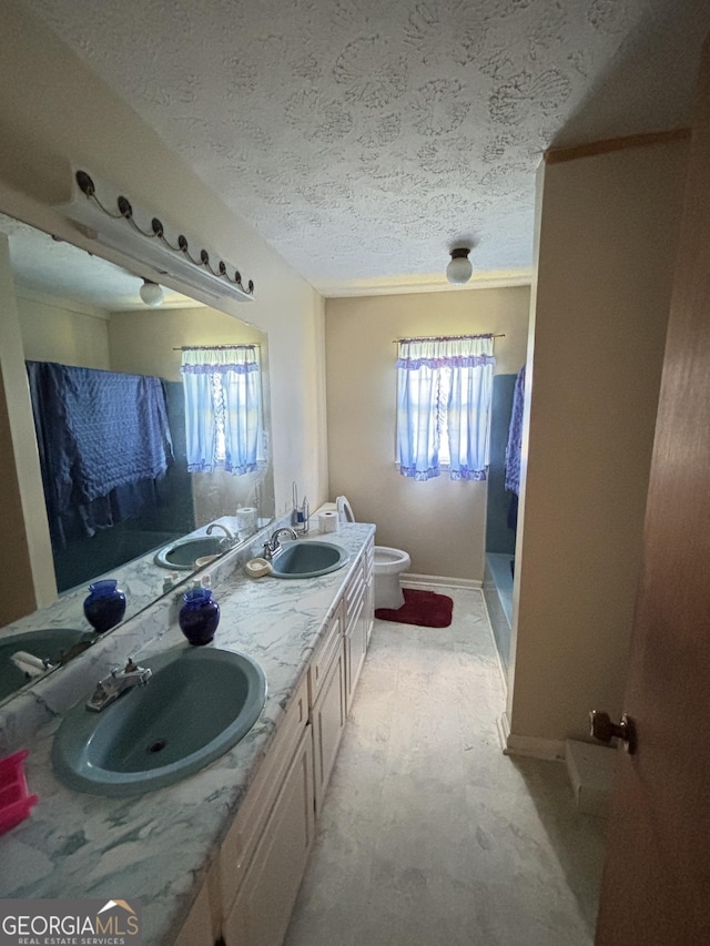 full bath with toilet, a shower with shower curtain, a textured ceiling, double vanity, and baseboards