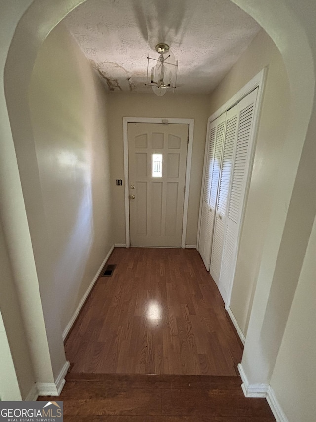 doorway with wood finished floors, arched walkways, baseboards, a chandelier, and a textured ceiling