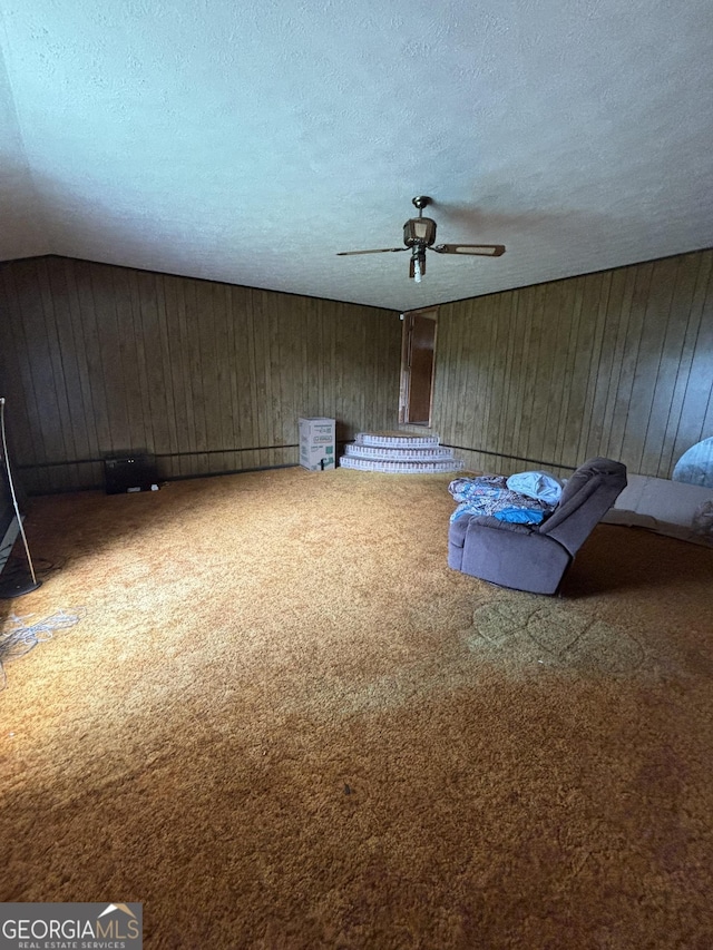 unfurnished living room with carpet flooring, ceiling fan, a textured ceiling, and wood walls