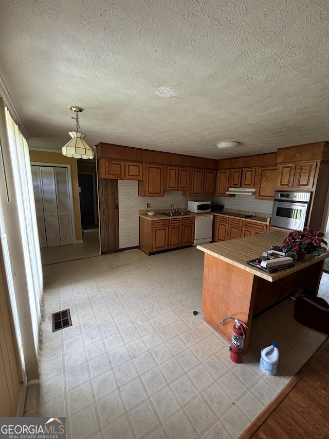 kitchen featuring white appliances, brown cabinetry, a textured ceiling, pendant lighting, and a peninsula