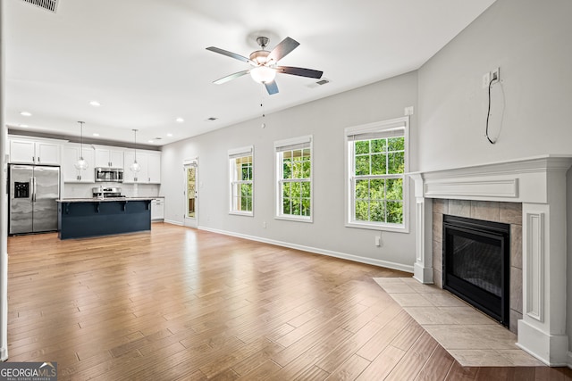 126 Ashton Pl, Newnan, GA 30265 - unfurnished living room featuring a tiled fireplace, light wood-type flooring, visible vents, baseboards, and ceiling fan