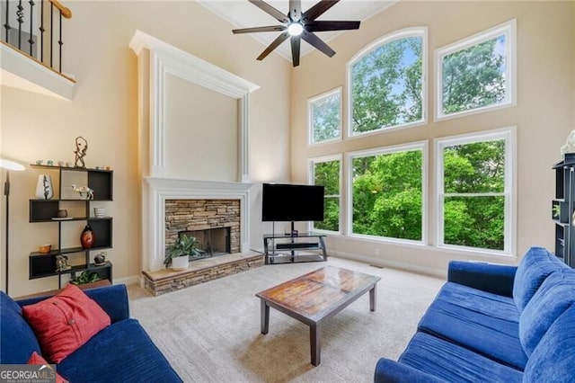 carpeted living room with a ceiling fan, a high ceiling, and a stone fireplace