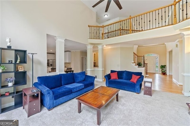 carpeted living room featuring high vaulted ceiling, a ceiling fan, ornate columns, stairway, and baseboards
