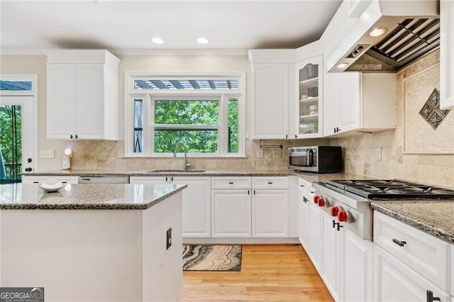 kitchen featuring stainless steel appliances, a sink, wall chimney exhaust hood, white cabinets, and ornamental molding