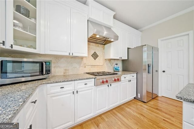 kitchen featuring stainless steel appliances, ornamental molding, white cabinetry, wall chimney exhaust hood, and light wood-type flooring