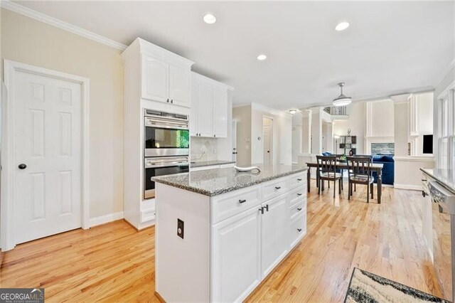kitchen with appliances with stainless steel finishes, light wood-type flooring, white cabinetry, ornamental molding, and a kitchen island