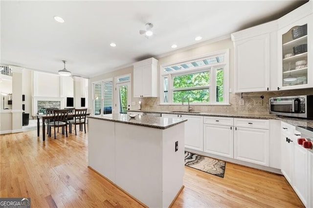 kitchen with stainless steel microwave, a sink, a kitchen island, backsplash, and white cabinets