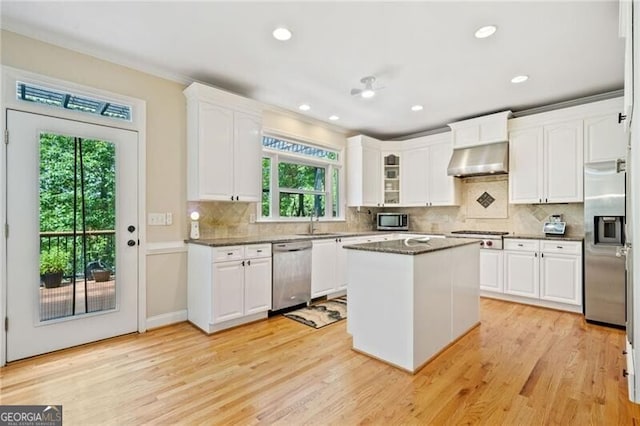kitchen featuring appliances with stainless steel finishes, under cabinet range hood, white cabinets, light wood finished floors, and decorative backsplash