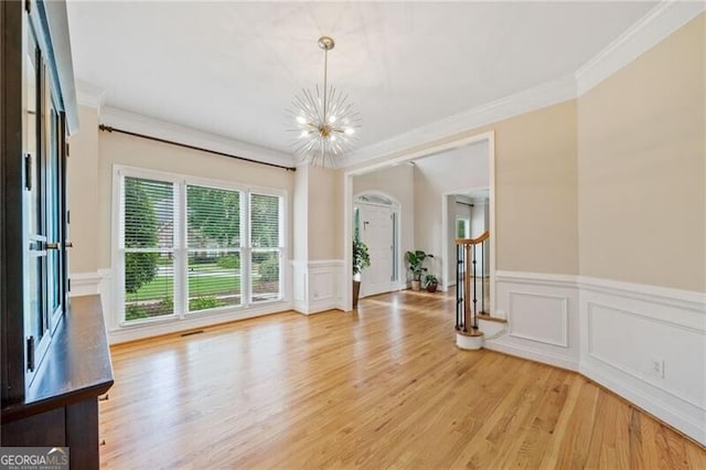 unfurnished dining area featuring a chandelier, light wood-type flooring, ornamental molding, wainscoting, and a decorative wall