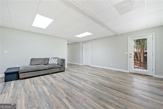 living area featuring a drop ceiling, wood finished floors, and baseboards