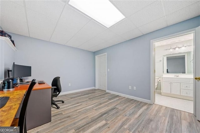 office area with wood finished floors, a drop ceiling, a sink, and baseboards