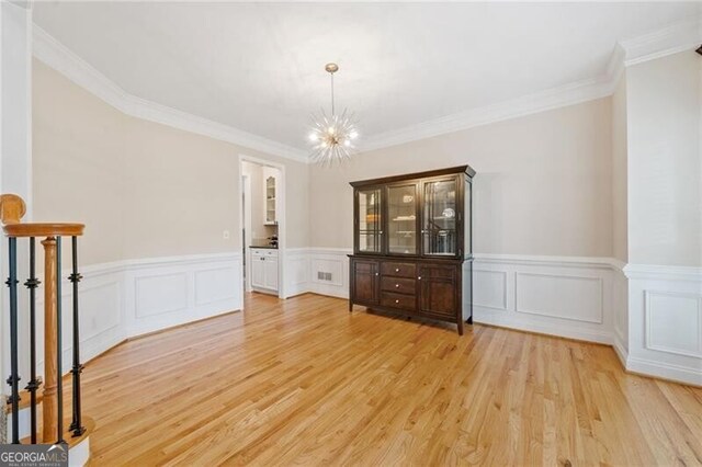 unfurnished dining area featuring light wood-type flooring, a chandelier, wainscoting, crown molding, and a decorative wall