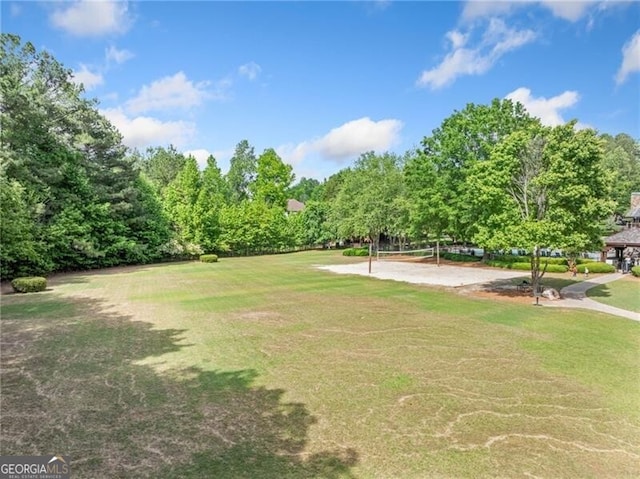 view of property's community featuring volleyball court, a lawn, and view of wooded area