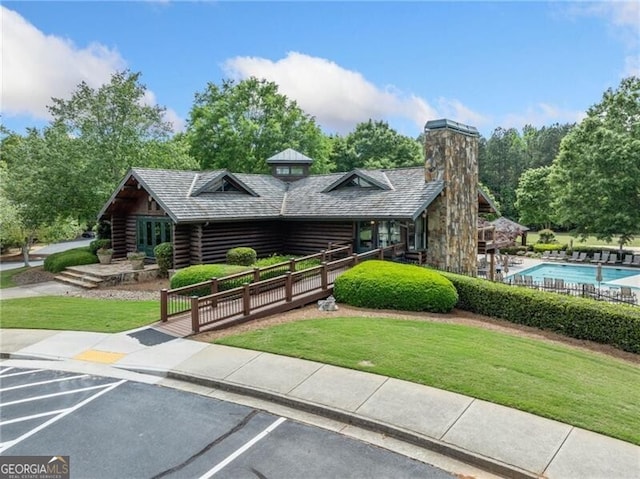 view of front of home with log exterior, uncovered parking, a front yard, and a chimney