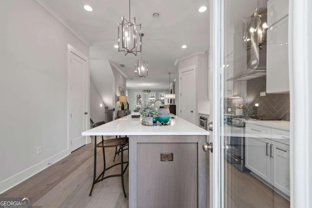 kitchen featuring light wood finished floors, a kitchen bar, a large island with sink, decorative backsplash, and a chandelier