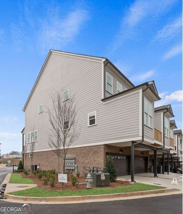 view of side of property featuring an attached garage, brick siding, and central AC