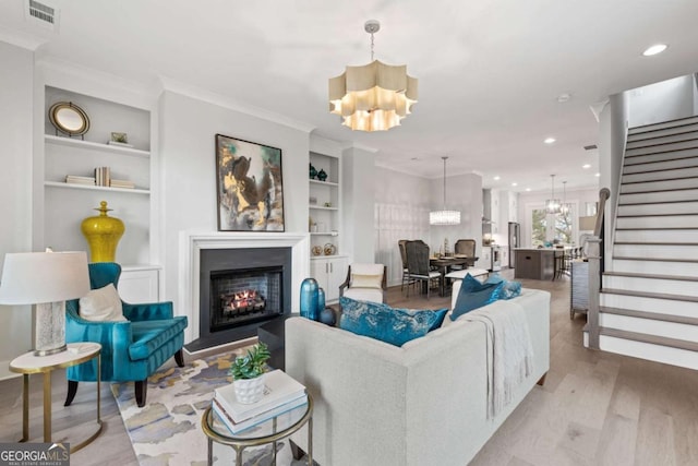 living room featuring an inviting chandelier, a lit fireplace, visible vents, built in features, and stairs