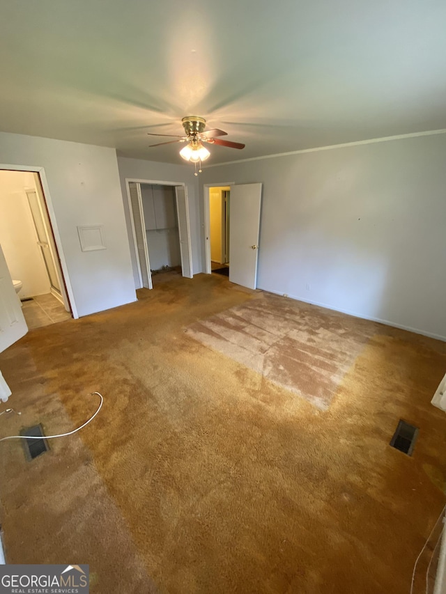 unfurnished bedroom with carpet flooring, a closet, a ceiling fan, and ensuite bath