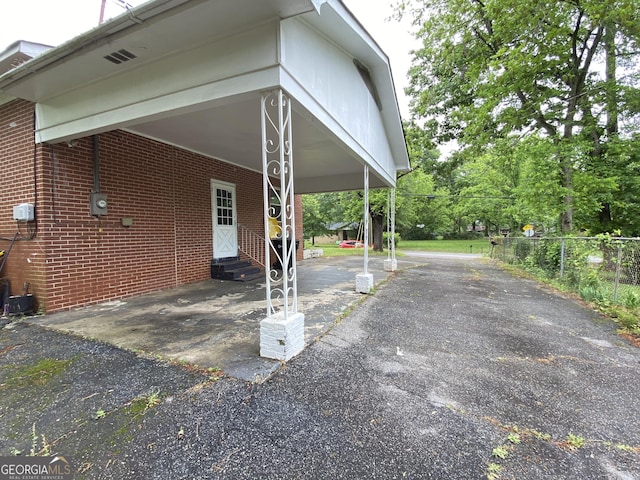 view of side of property featuring entry steps, driveway, fence, brick siding, and an attached carport