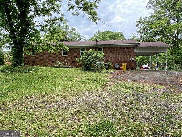 rear view of property featuring crawl space, a carport, driveway, brick siding, and a lawn
