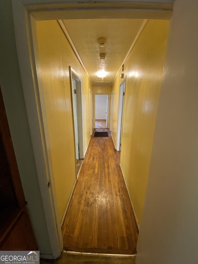 corridor with crown molding, dark wood-style floors, and wooden walls