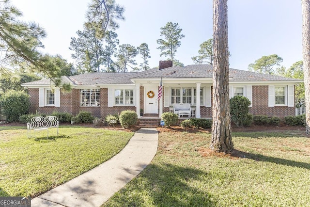 ranch-style home with a porch, a front lawn, a chimney, and brick siding