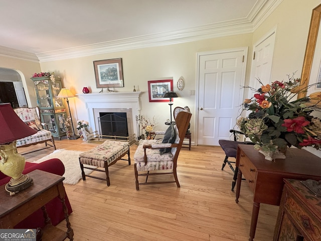 living room featuring light wood-style floors, a fireplace, ornamental molding, and arched walkways
