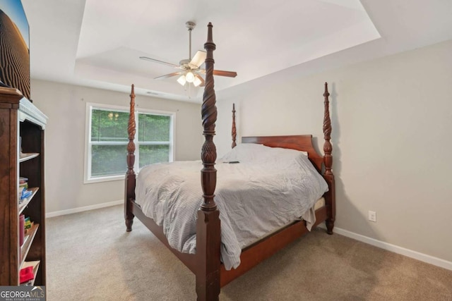 bedroom with a tray ceiling, carpet floors, baseboards, and a ceiling fan