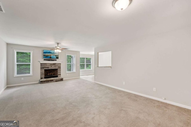 unfurnished living room featuring a ceiling fan, a stone fireplace, baseboards, and carpet