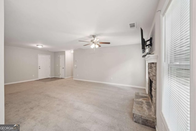 unfurnished living room with a ceiling fan, a stone fireplace, visible vents, and carpet floors