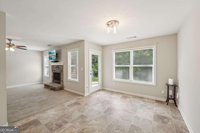 unfurnished living room featuring a wealth of natural light, visible vents, a fireplace, and ceiling fan