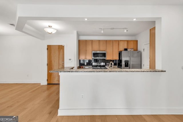 kitchen featuring stainless steel appliances, light wood-type flooring, baseboards, light stone countertops, and decorative backsplash