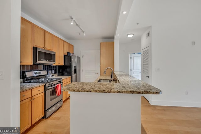 kitchen featuring a peninsula, a sink, stainless steel appliances, light wood-type flooring, and light stone countertops