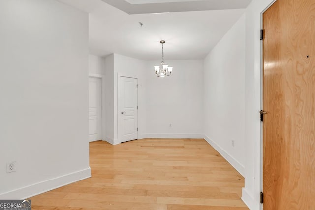 unfurnished dining area with baseboards, a notable chandelier, and light wood-type flooring
