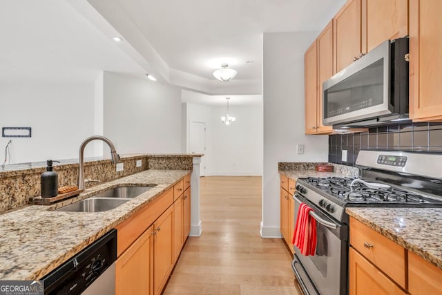 kitchen with appliances with stainless steel finishes, light stone counters, a sink, decorative backsplash, and light wood-type flooring
