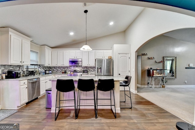 kitchen featuring stainless steel appliances, lofted ceiling, arched walkways, white cabinetry, and decorative backsplash